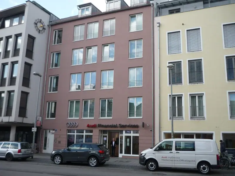 Straßenfront mehrerer Stadthäuser mit Fensterreihen, davor ein weißer Transporter