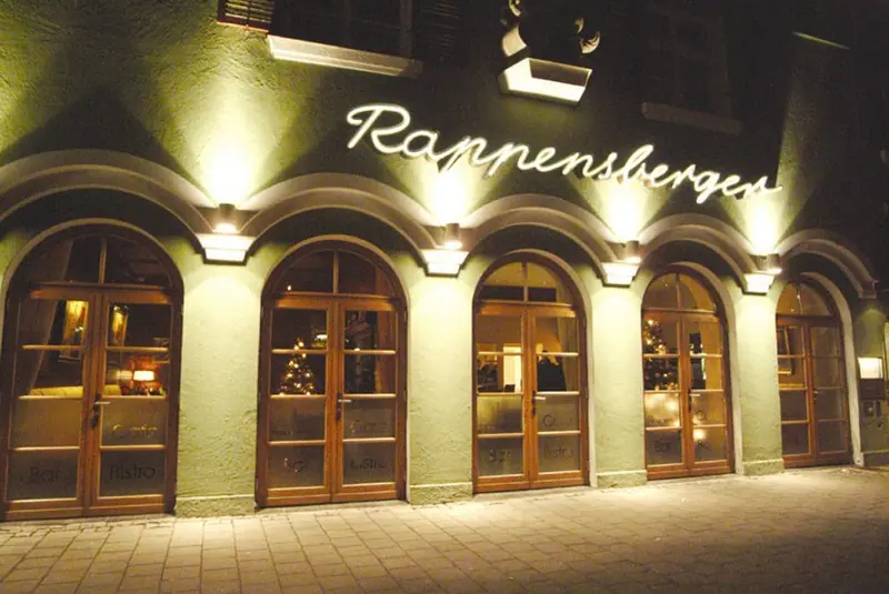 Beleuchtete Bogenfenster und Holztüren an einer grünen Fassade am Abend