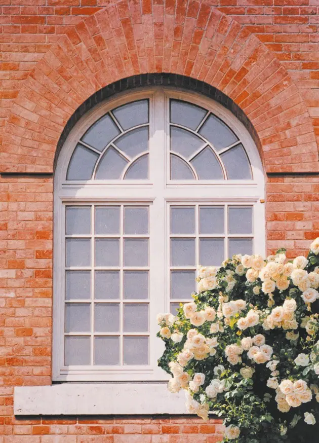 Weißes Rundbogenfenster mit Sprossen in einer roten Backsteinwand